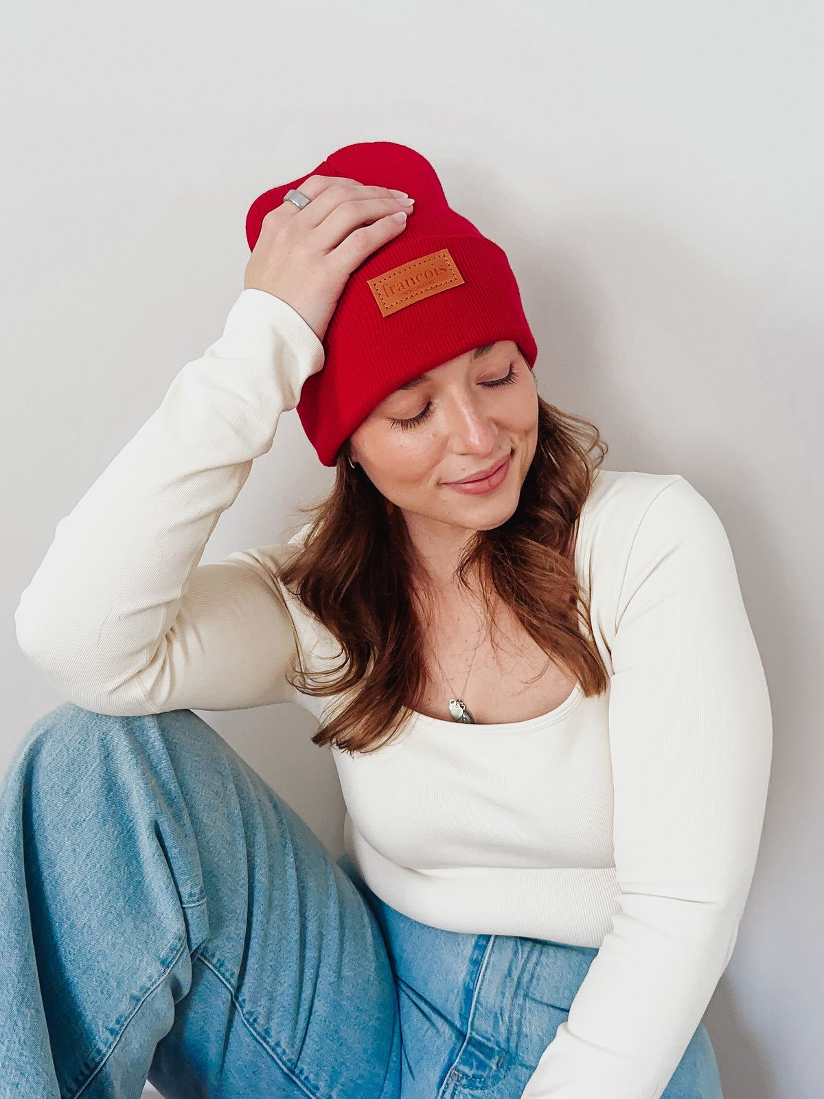 Woman wearing a red beanie with a brand logo against a plain background