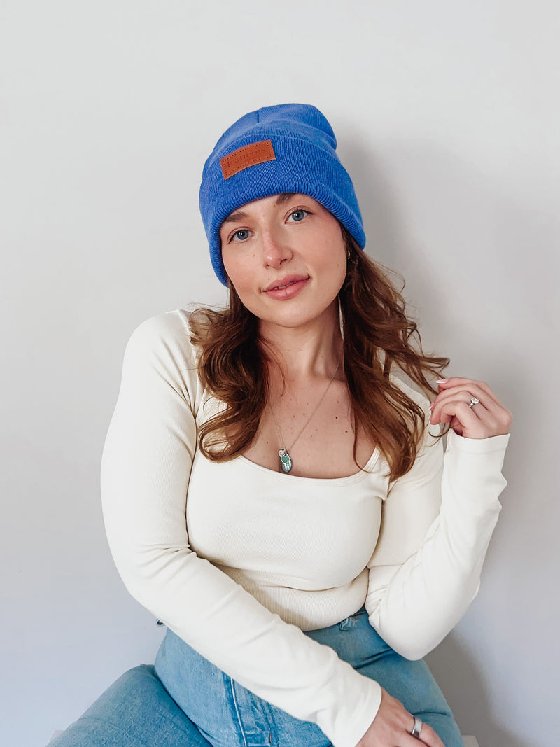 Woman wearing a blue beanie with a brown patch on a plain background