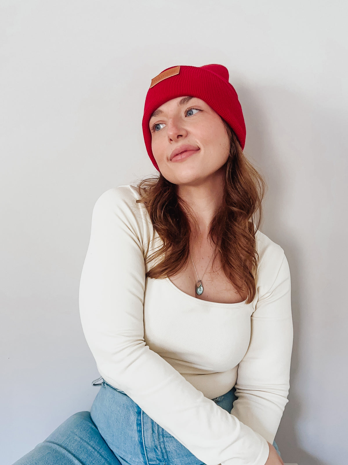 Woman wearing a red beanie and white long-sleeve shirt against a plain background