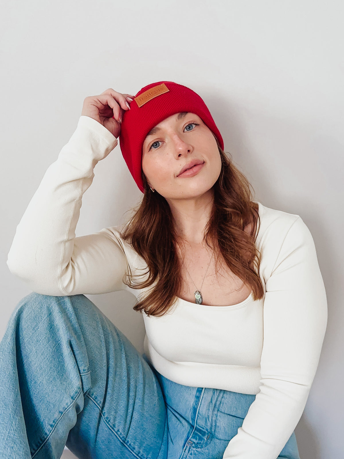 Woman wearing a red beanie and white sweater against a plain background