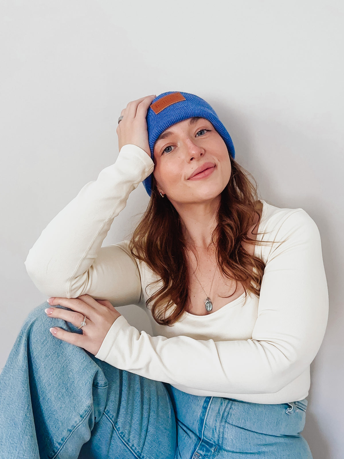 Woman wearing a blue beanie with brown leather patch on a light gray background